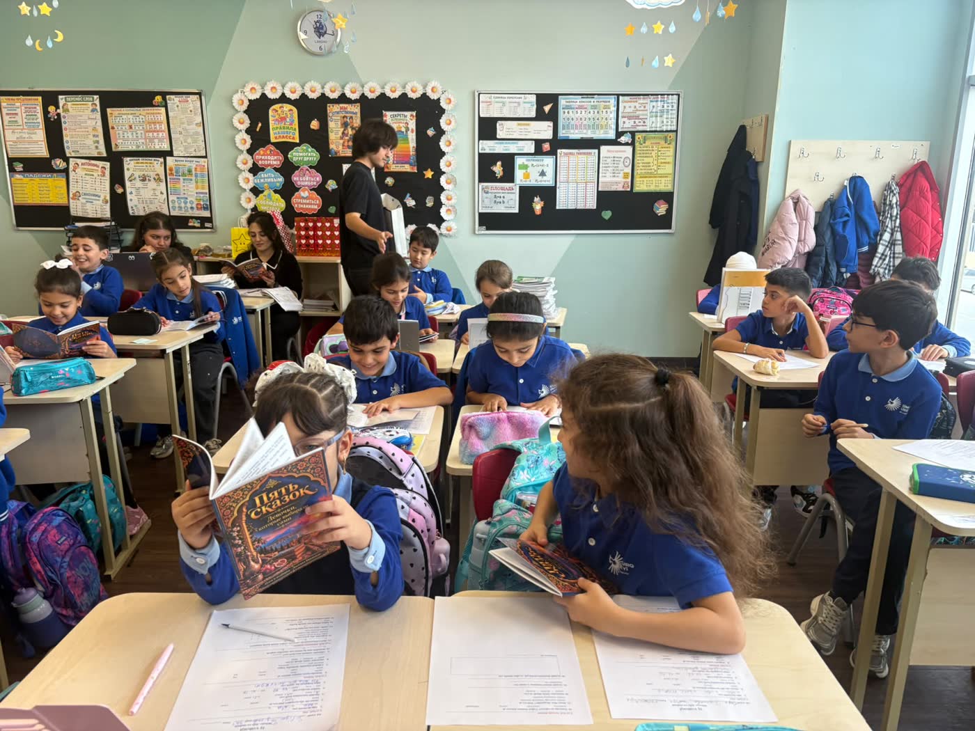 Two girls at the front desk, one reading the book held up to her face, while Jamal hands out books behind them.